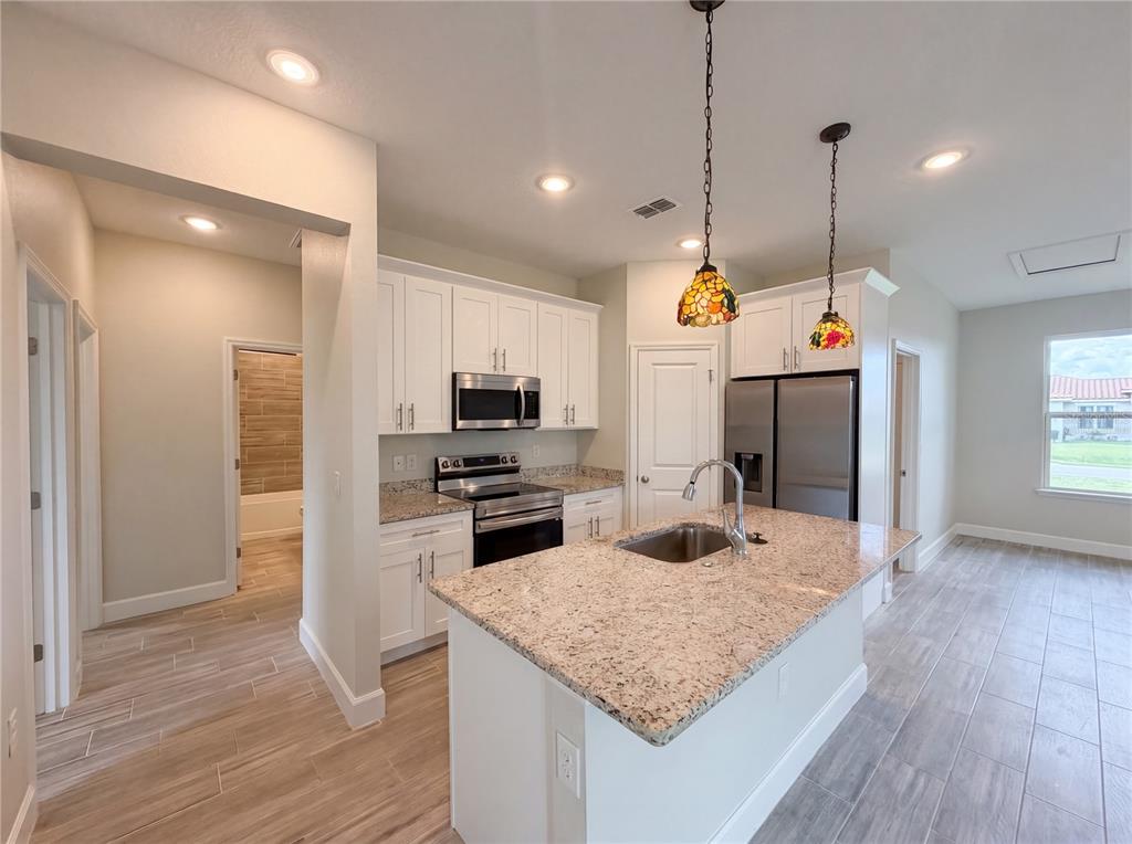 A kitchen features white cabinets, granite countertops, a center island, and stainless steel appliances — 446 CINNAMON DRIVE, KISSIMMEE, FL