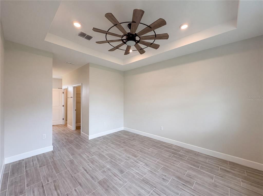 An empty room features light gray walls, wood-look tile flooring, and a tray ceiling — 446 CINNAMON DRIVE, KISSIMMEE, FL
