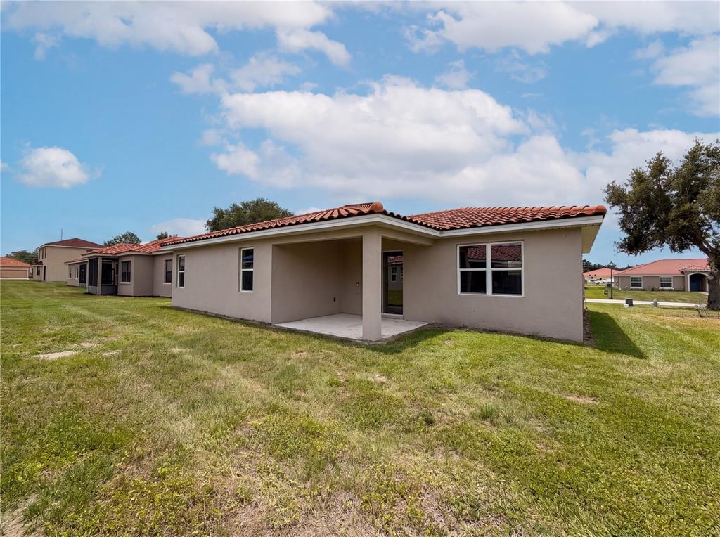 The rear exterior of a single-story house features a covered patio and a tiled roof — 446 CINNAMON DRIVE, KISSIMMEE, FL