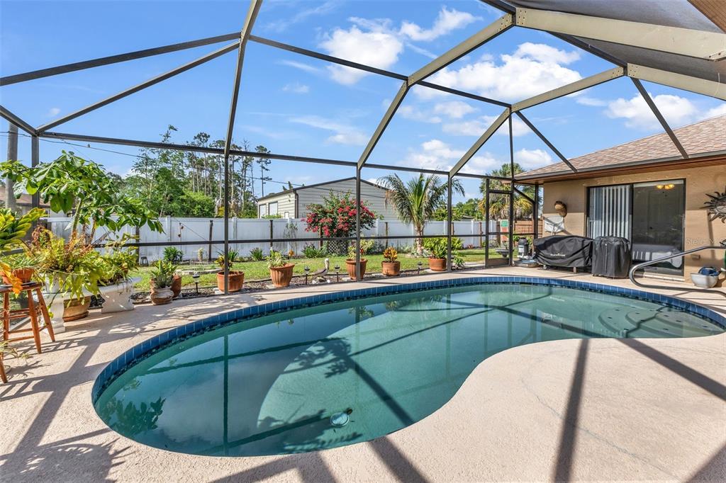 A swimming pool sits inside a screened-in lanai with a patio and potted plants — 23345 FERNDALE AVENUE, PUNTA GORDA, FL