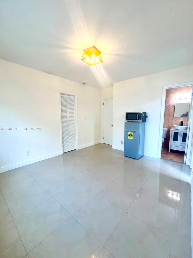 A room with white walls, tile flooring, a small refrigerator, and an adjacent bathroom — HOLLYWOOD, FL