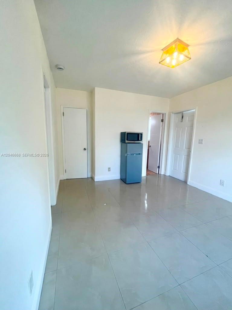 A room with light-colored walls, tile flooring, a small refrigerator, and a ceiling light fixture — HOLLYWOOD, FL