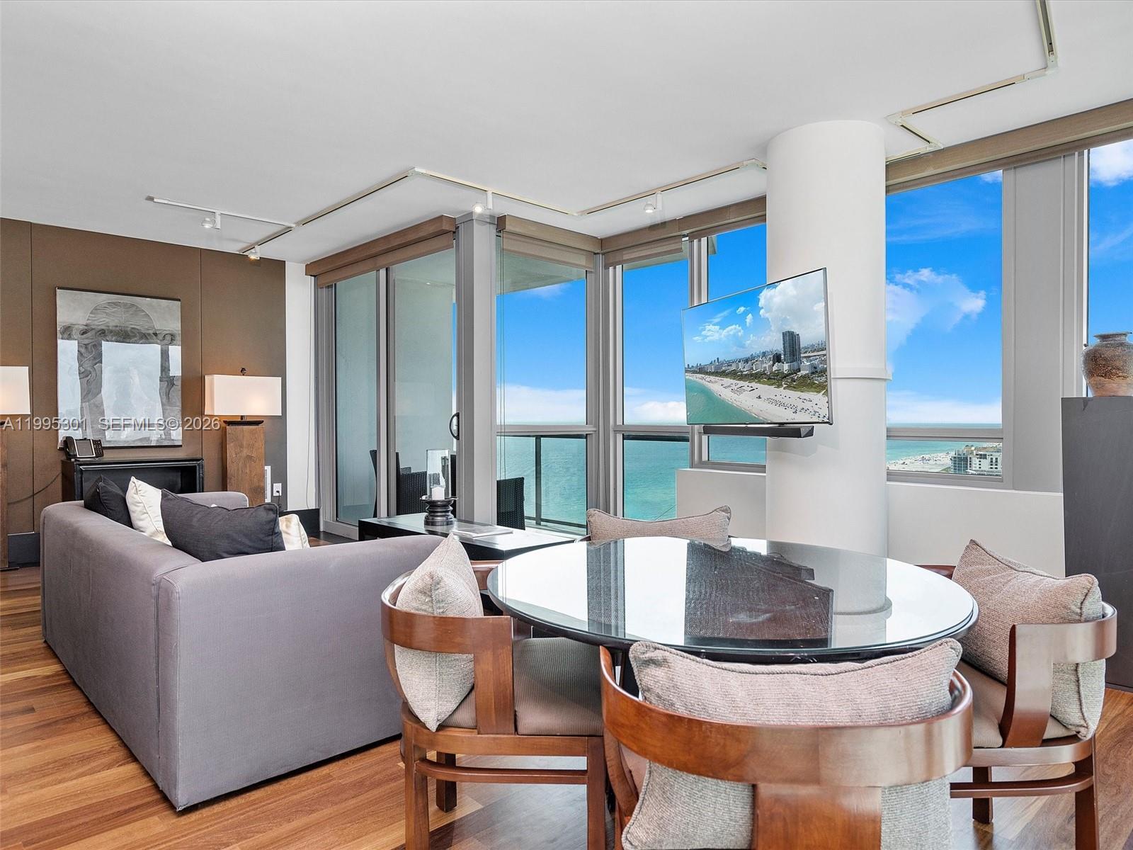A living and dining area features a glass table, gray sofa, and floor-to-ceiling ocean views — 101 20th St # 3302, Miami Beach FL 33139, MIAMI BEACH, FL