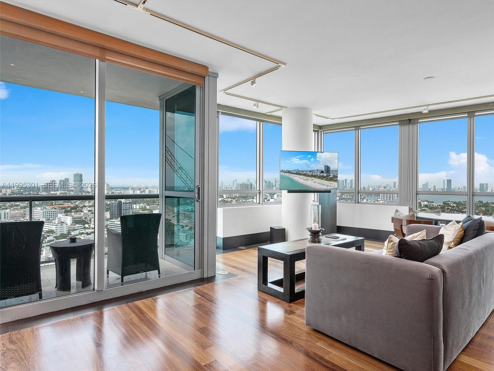 A living room with hardwood floors, floor-to-ceiling windows, and a balcony overlooking a city skyline — 101 20th St # 3302, Miami Beach FL 33139, MIAMI BEACH, FL
