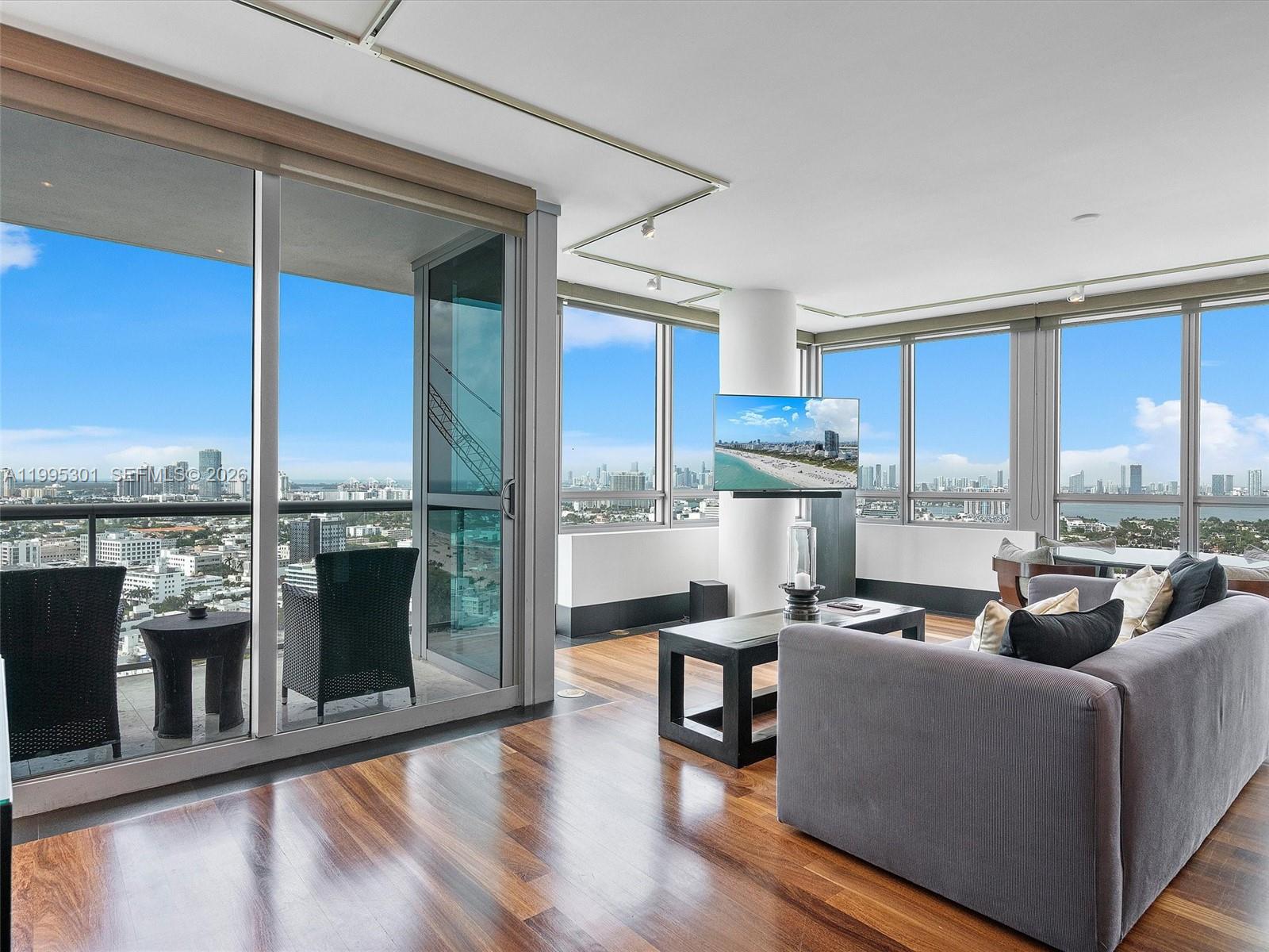 A living room with hardwood floors, floor-to-ceiling windows, and a balcony overlooking a city skyline — 101 20th St # 3302, Miami Beach FL 33139, MIAMI BEACH, FL