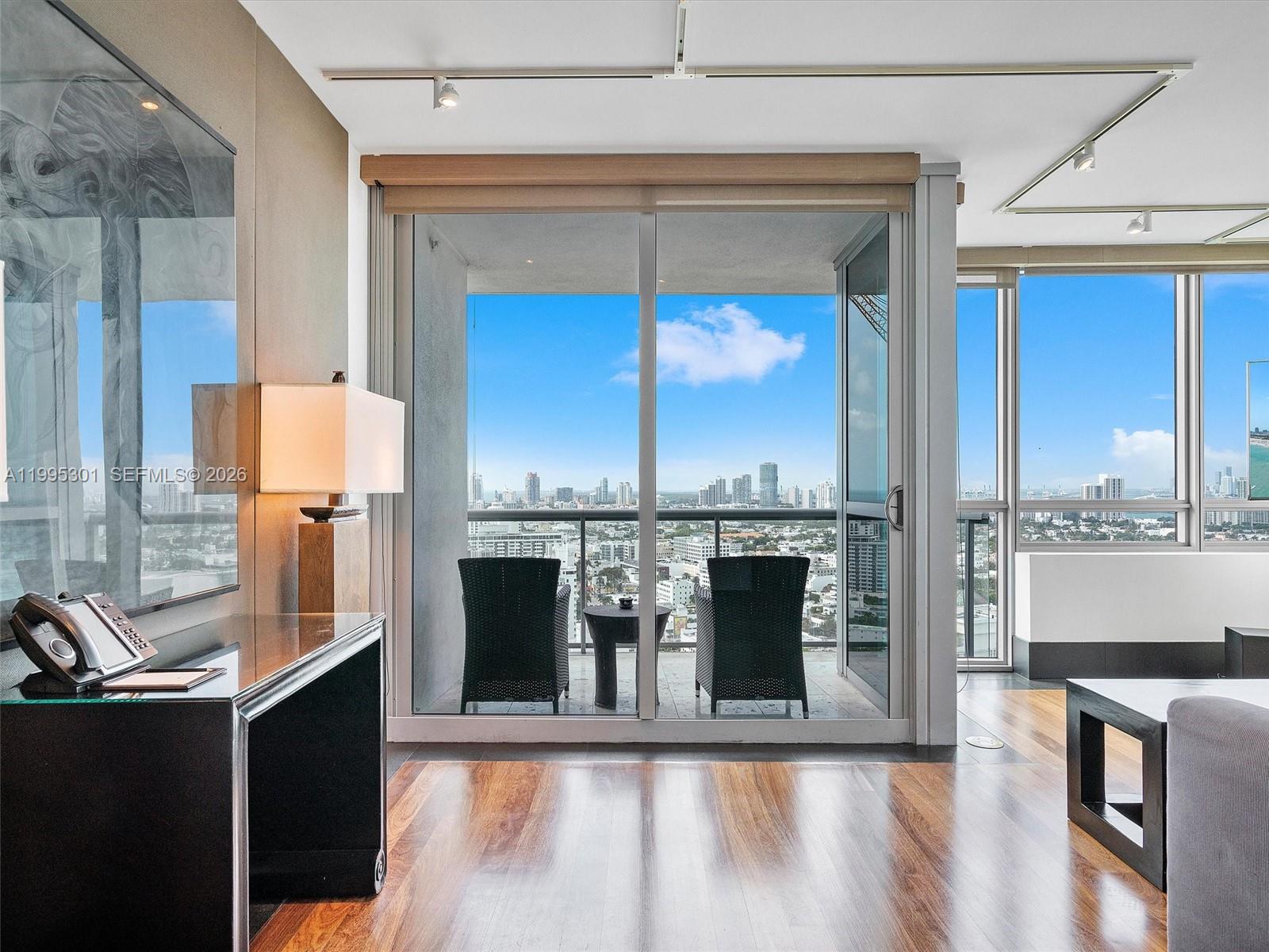A modern room with hardwood floors features a desk, a lamp, and a balcony view — 101 20th St # 3302, Miami Beach FL 33139, MIAMI BEACH, FL