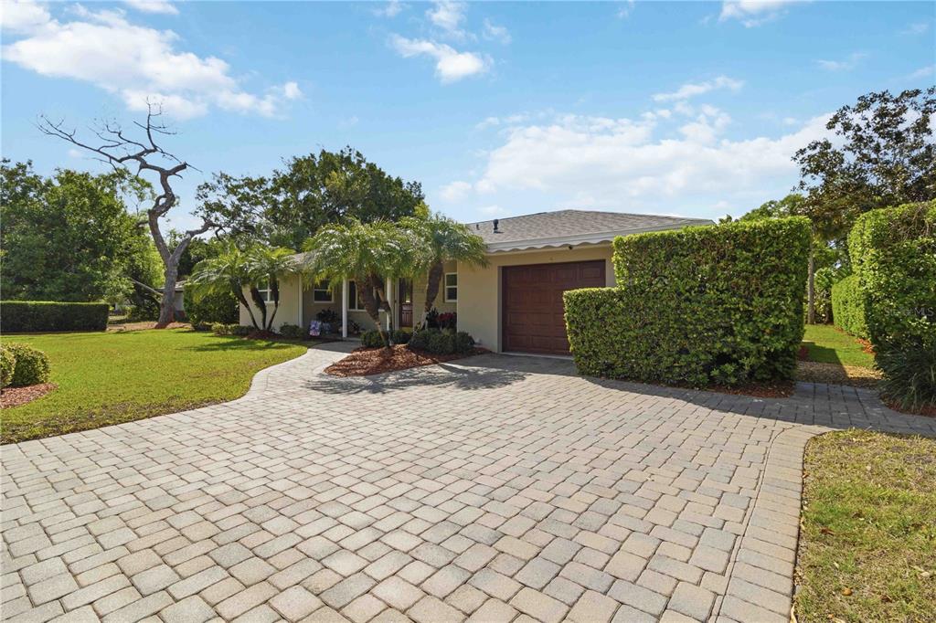 A single-story house with a paved driveway, a garage, and manicured hedges under a blue sky — 2068 SUNNYSIDE LANE, SARASOTA, FL