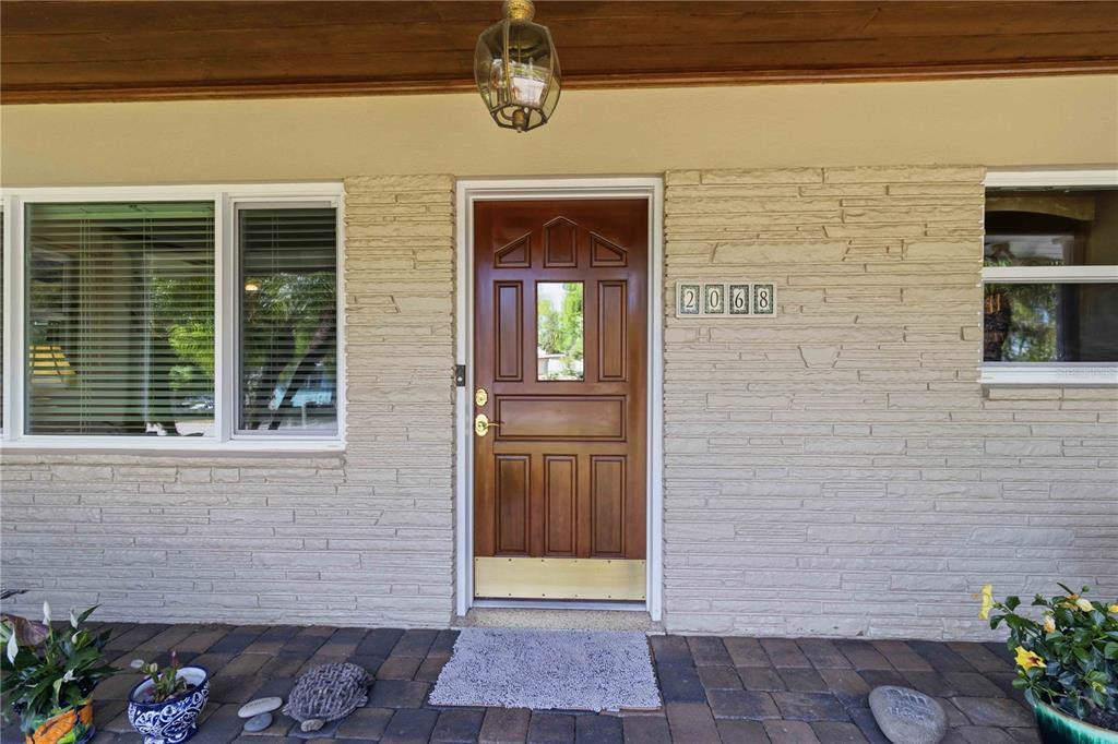A front porch with a wooden door, stone-textured siding, and a hanging light fixture — 2068 SUNNYSIDE LANE, SARASOTA, FL