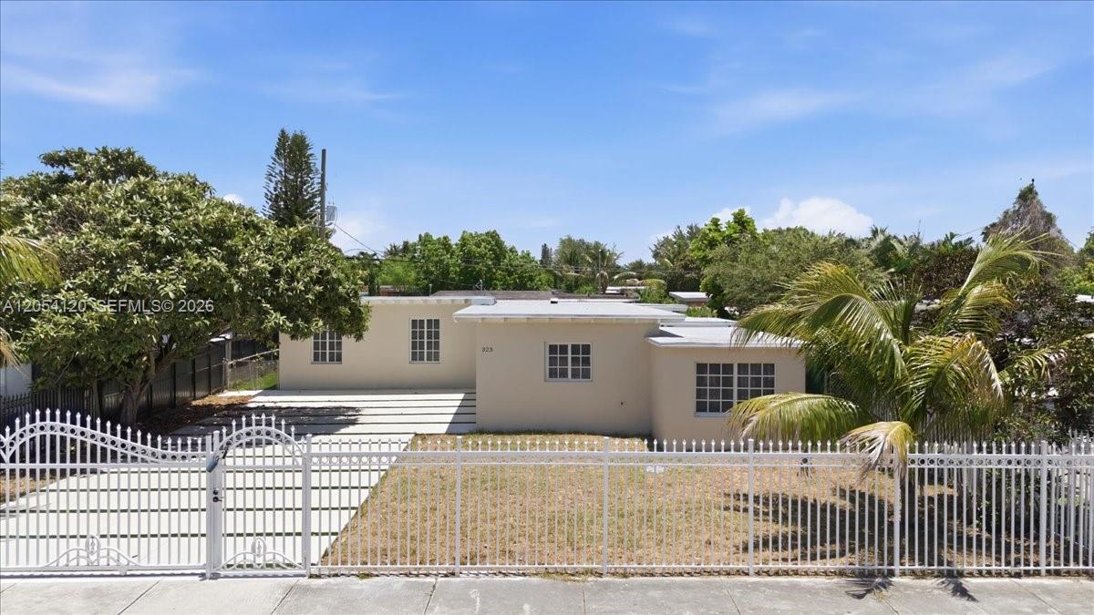 A single-story house with a flat roof, beige stucco walls, and a white metal fence — 323 NW 104th Ter, Miami FL 33150, MIAMI, FL