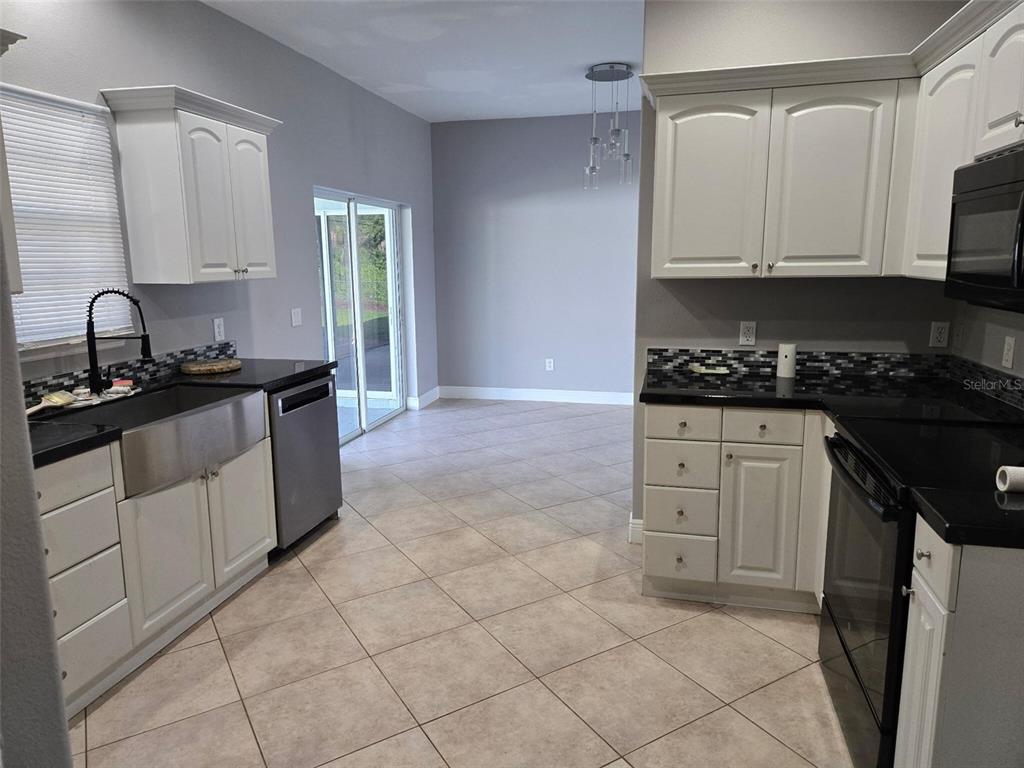 A kitchen features white cabinets, black countertops, a stainless steel farmhouse sink, and tile flooring — 2739 ATWATER DRIVE, NORTH PORT, FL