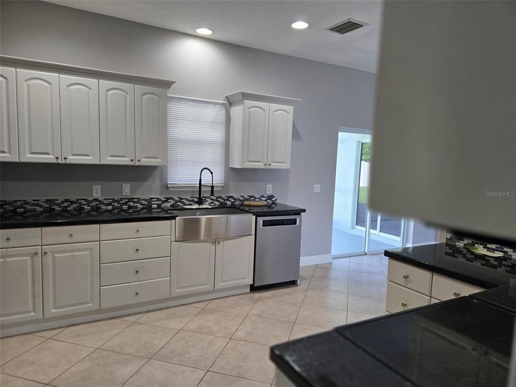 A kitchen features white cabinetry, black countertops, a stainless steel farmhouse sink, and tile flooring — 2739 ATWATER DRIVE, NORTH PORT, FL