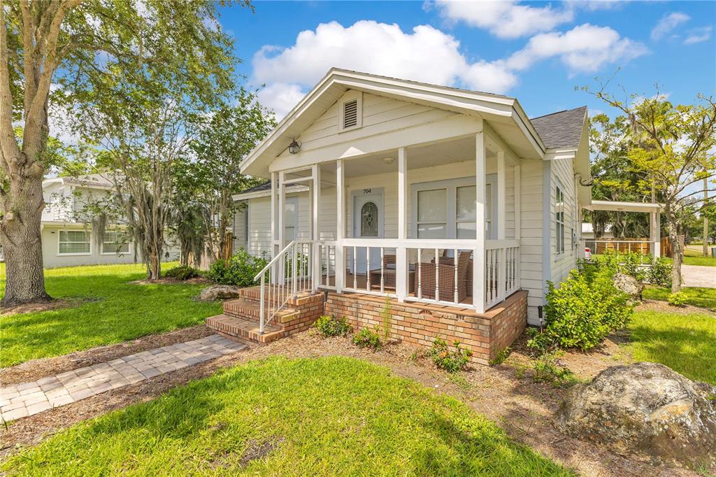 A white cottage with a screened front porch, brick foundation, and a stone walkway — 704 S CLYDE AVENUE, KISSIMMEE, FL