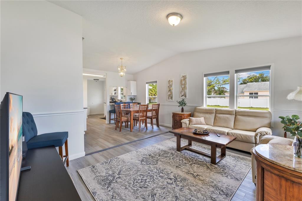 A living room and dining area feature light wood flooring, white walls, and neutral furniture — 704 S CLYDE AVENUE, KISSIMMEE, FL