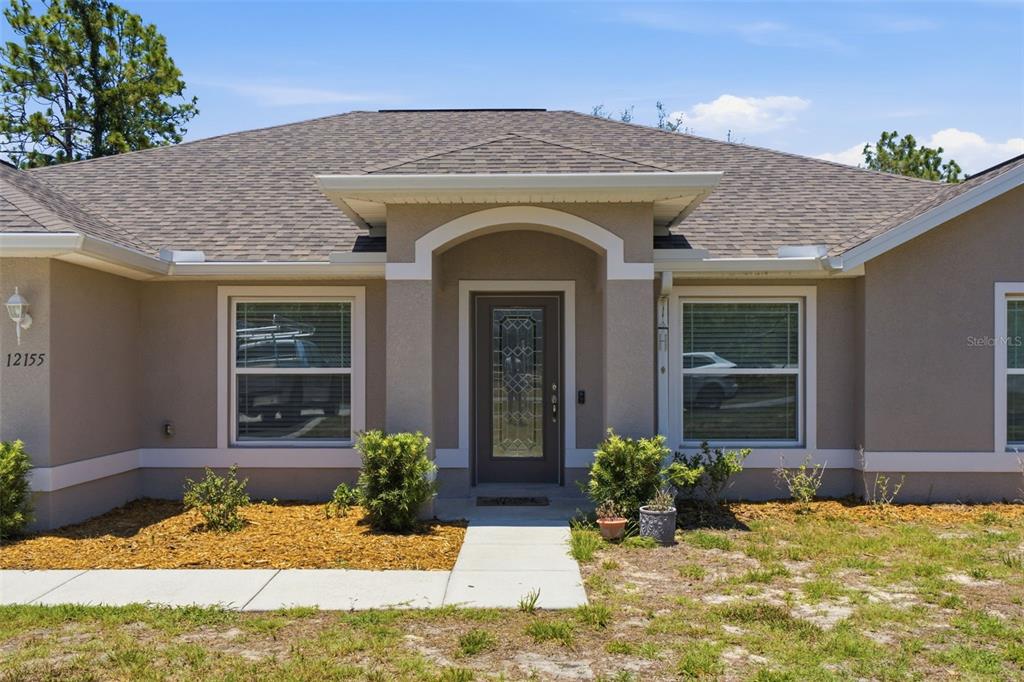 A single-story house with a beige stucco exterior, a gray shingled roof, and a front entrance — 12155 PEREGRINE FALCON AVENUE, WEEKI WACHEE, FL