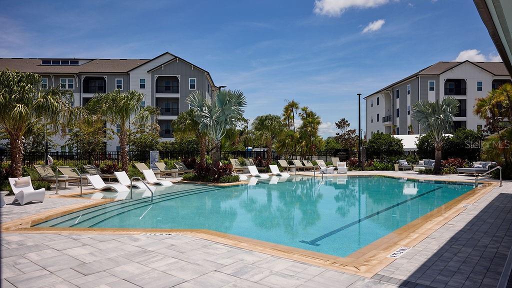 A swimming pool with lounge chairs sits between two multi-story apartment buildings under a sky — 9500 GRANDTREE AVENUE UNIT C1, VENICE, FL