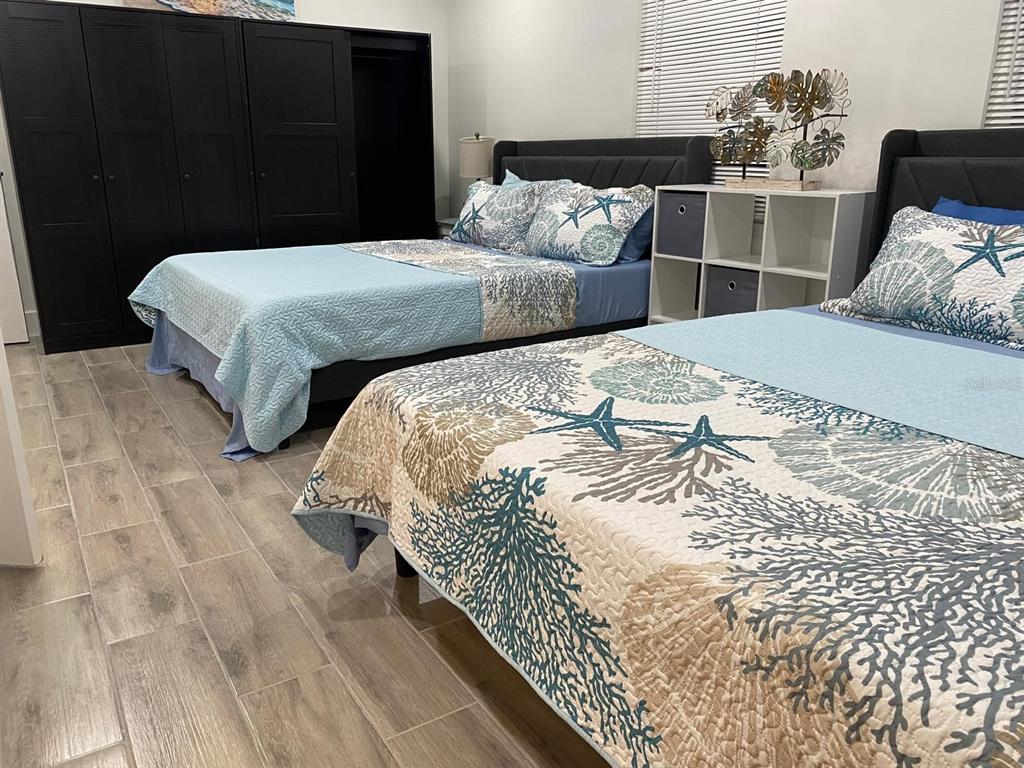 A bedroom features two beds with coastal-themed bedding, a black wardrobe, and light tile flooring — 9921 VAUGHN STREET UNIT 3 Bd, GIBSONTON, FL