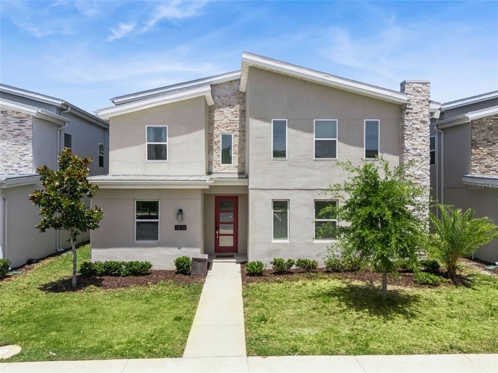 A two-story house with a beige stucco exterior, stone accents, and a red front door — 2876 SIMILE STREET, KISSIMMEE, FL