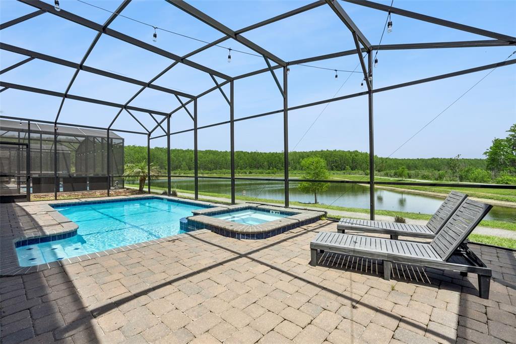 A screened-in pool and hot tub overlook a pond with lounge chairs on the patio — 2876 SIMILE STREET, KISSIMMEE, FL