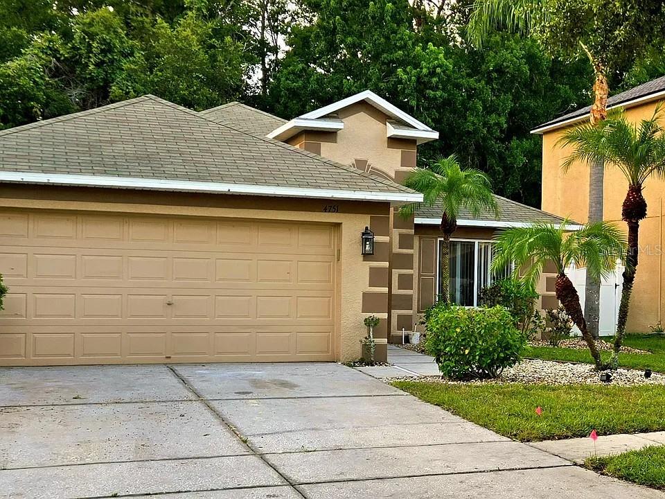 A single-story house with a tan stucco exterior, a two-car garage, and two palm trees — 4751 BARCHETTA, LAND O LAKES, FL