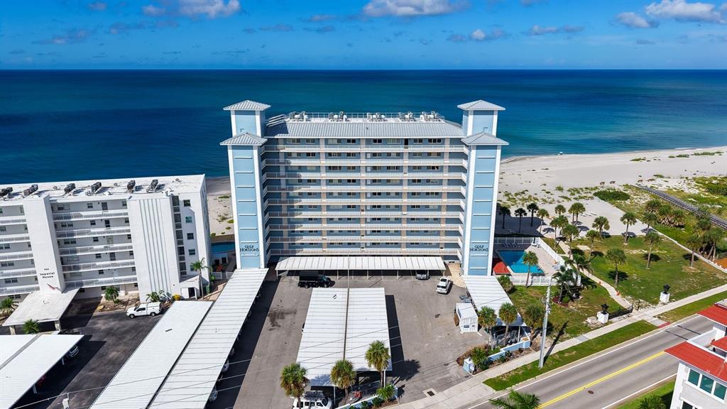 An aerial view shows a multi-story beachfront condominium building with covered parking and a pool — 555 THE ESPLANADE N UNIT 802, VENICE, FL