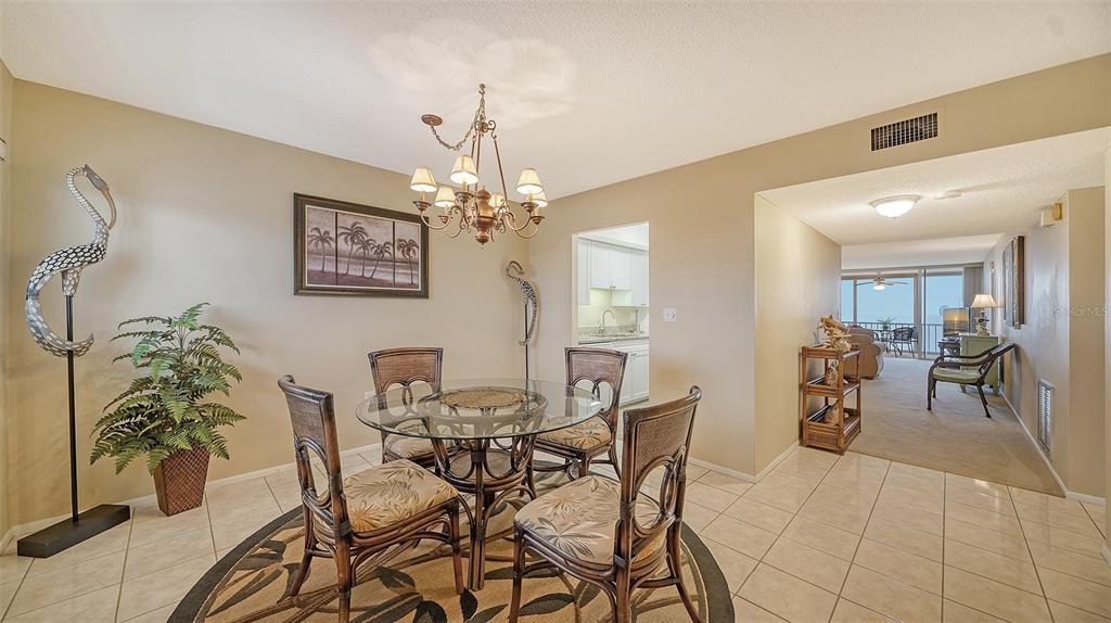 A dining area with a glass table, four chairs, and tile flooring leads to a balcony — 555 THE ESPLANADE N UNIT 802, VENICE, FL