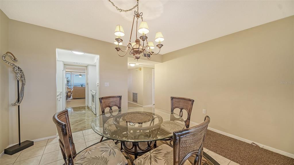 A dining area features a glass-topped table with four chairs under a chandelier — 555 THE ESPLANADE N UNIT 802, VENICE, FL
