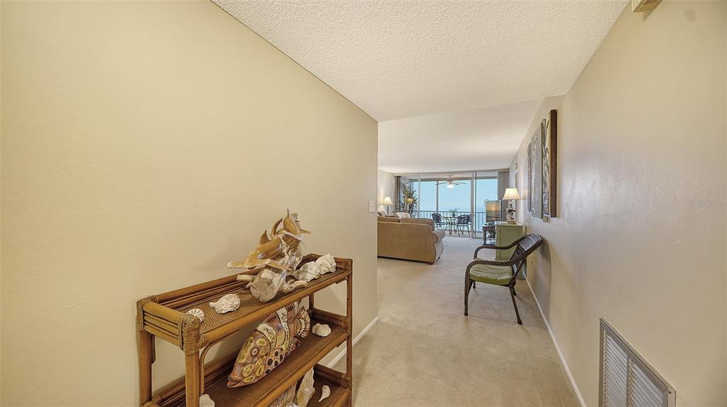 A hallway with a bamboo shelf leads into a living room with a balcony view — 555 THE ESPLANADE N UNIT 802, VENICE, FL