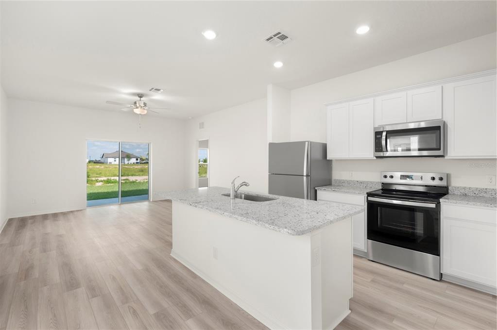 A kitchen with white cabinets, granite countertops, and stainless steel appliances opens to a living area — 3617 AMANATSU STREET, LAKE ALFRED, FL