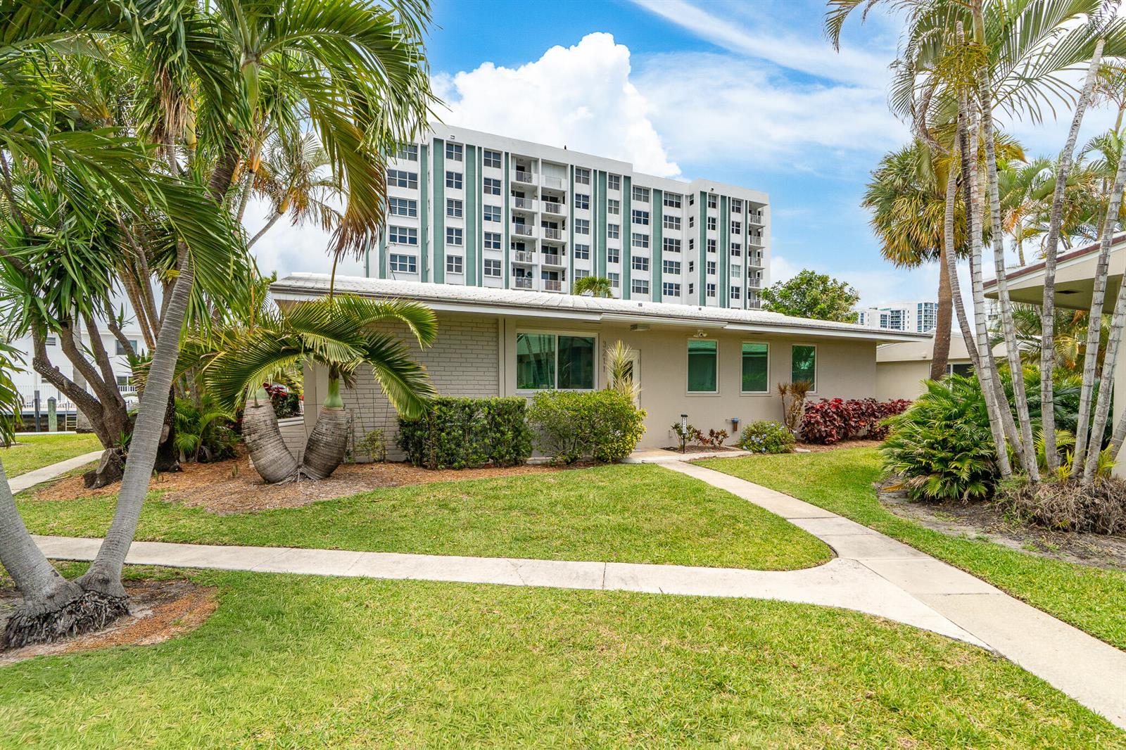 A single-story house with a light-colored exterior sits in front of a tall apartment building — 3211 SE 11th Street # 3e, Pompano Beach FL 33062, POMPANO BEACH, FL
