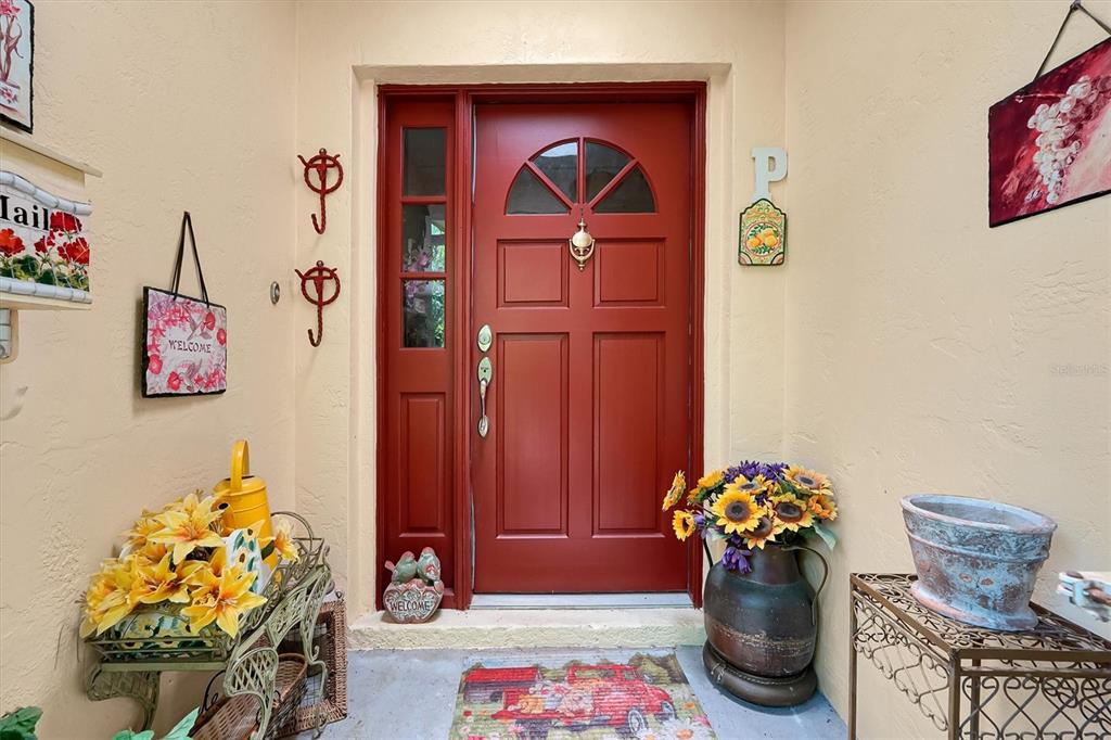 A red front door with a sidelight is decorated with flowers and welcome signs — 3640 WOOD DUCK DRIVE, MIMS, FL