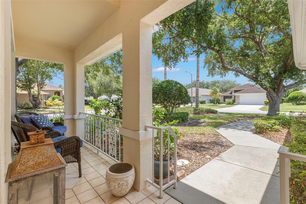 A covered front porch features tiled flooring, wicker chairs, and a view of the neighborhood — 14023 SHOAL DRIVE, HUDSON, FL