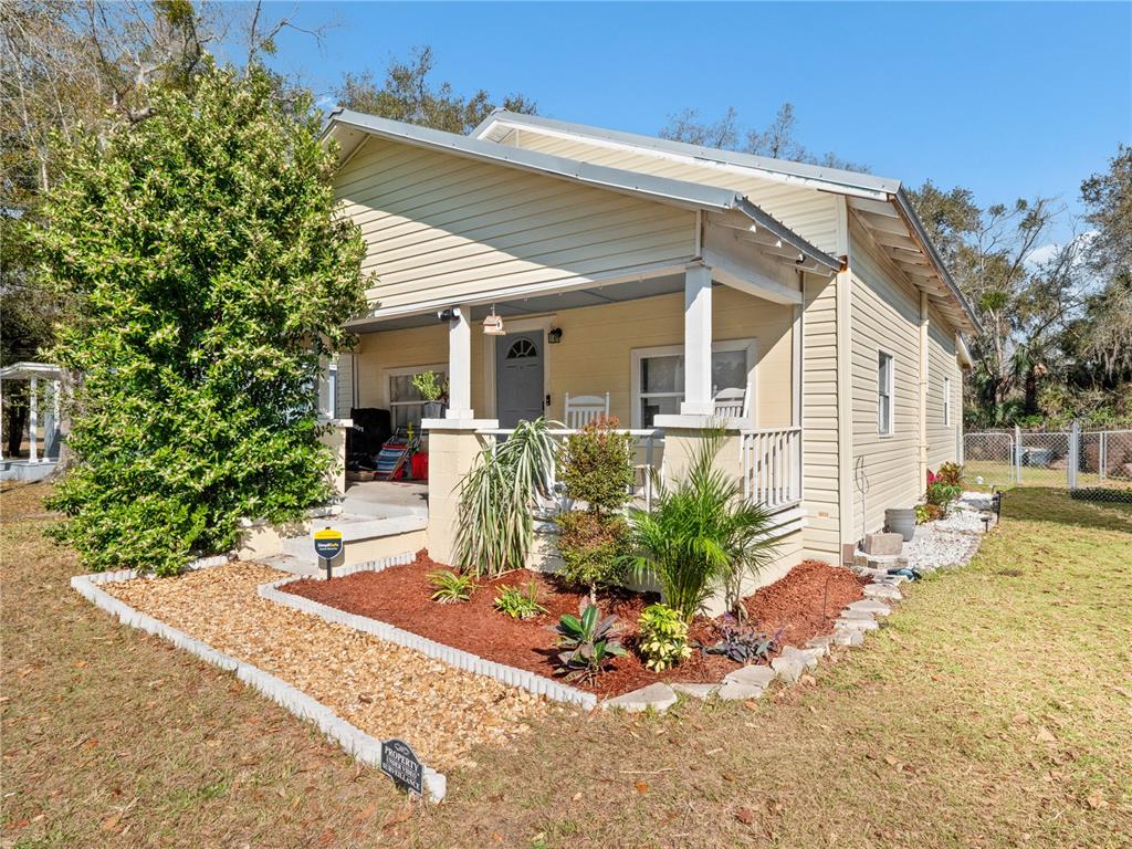 A light yellow house with a front porch and landscaped yard under a blue sky — 1208 W 10TH STREET, SANFORD, FL