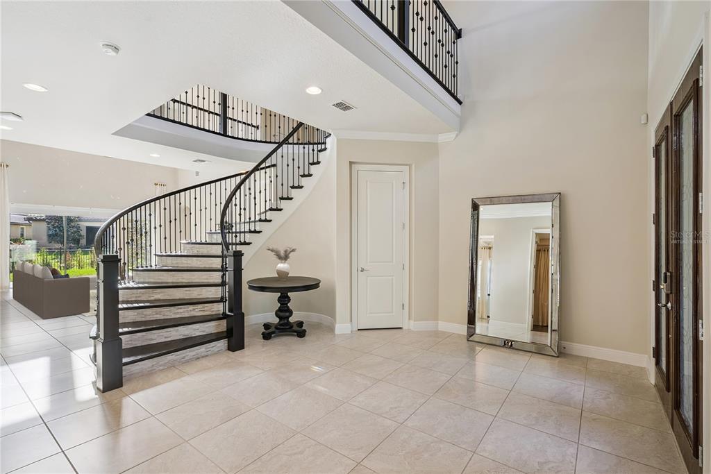 An entryway features a curved staircase with iron railings, tile flooring, and a large mirror — 8591 ADALINA PLACE, ORLANDO, FL