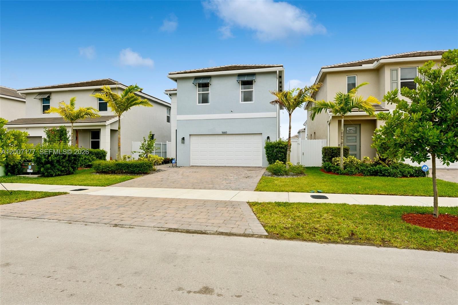 A light blue two-story house with a white garage door sits between two neighboring homes — 1660 SE 6th St, Homestead FL 33033, HOMESTEAD, FL