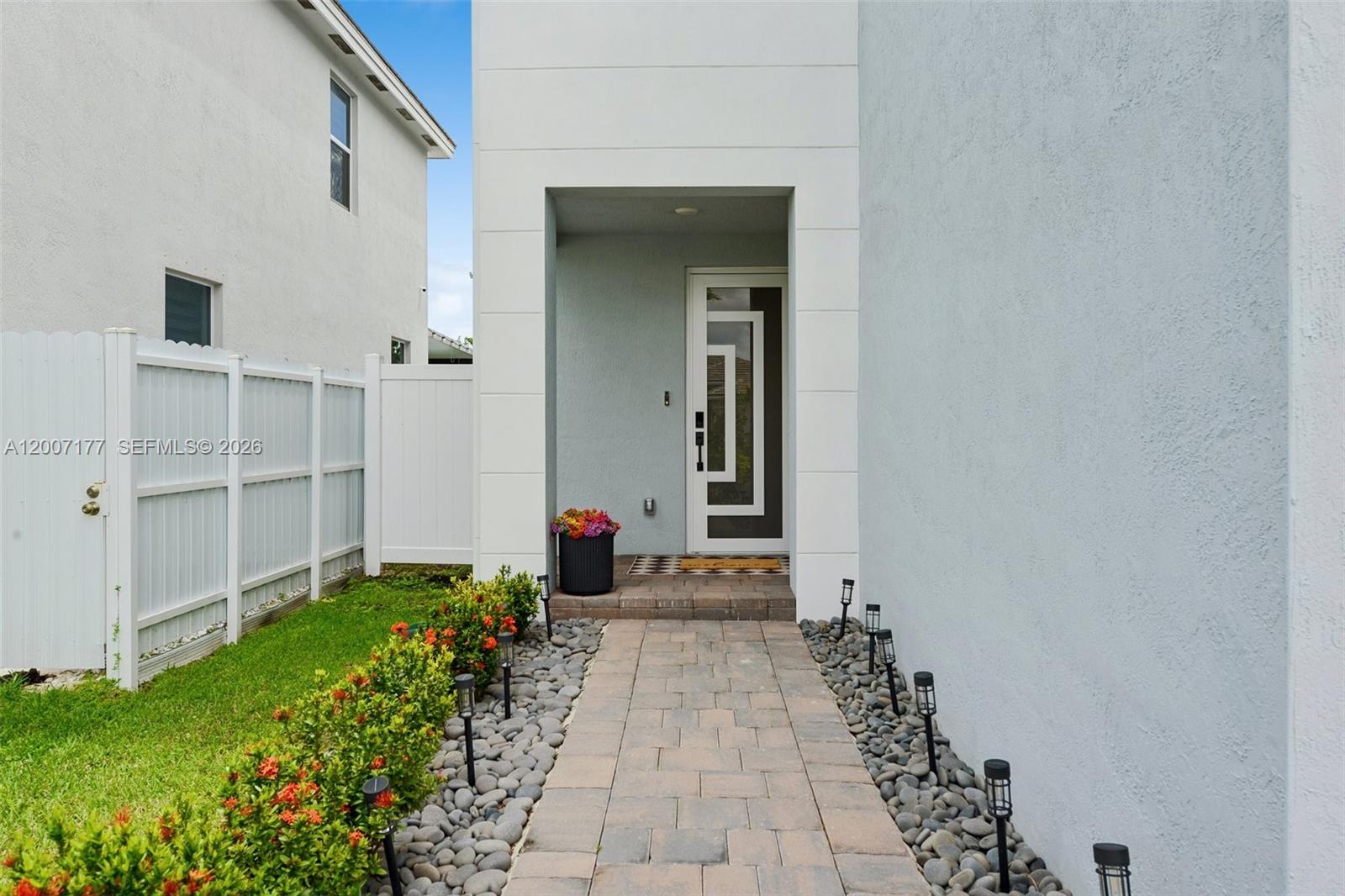 A paved walkway leads to the front entrance of a modern home with white siding — 1660 SE 6th St, Homestead FL 33033, HOMESTEAD, FL