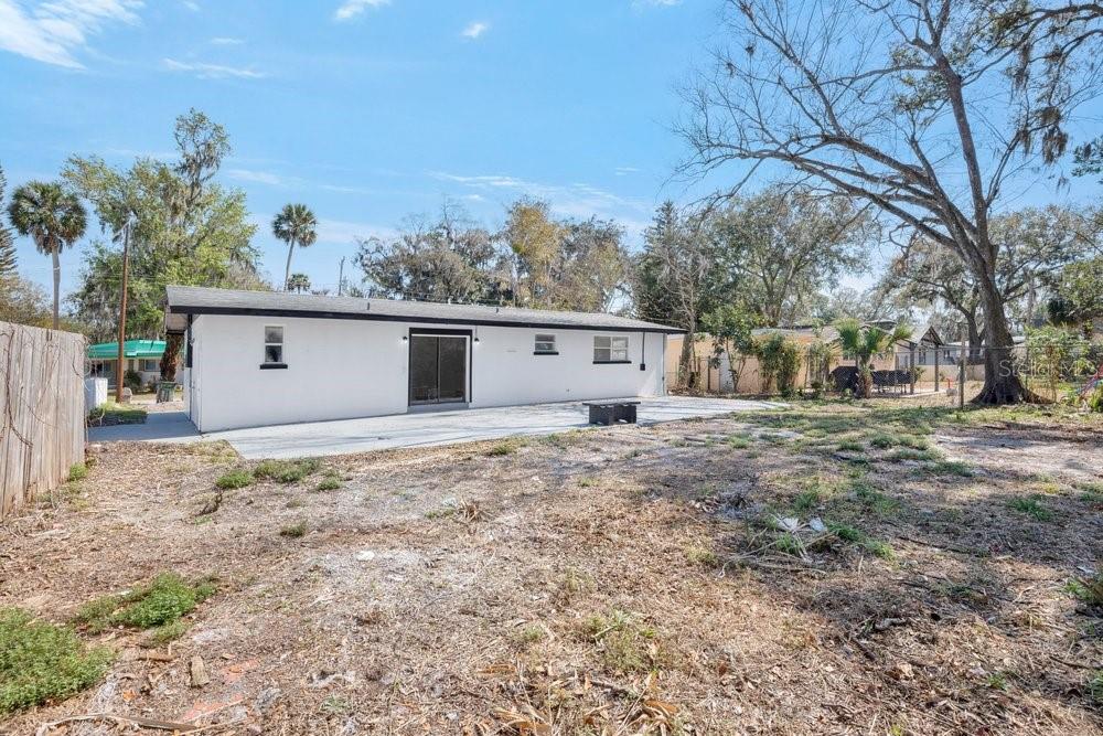 A white house with a concrete patio sits on a large, unlandscaped dirt backyard — 124 BAYWOOD DRIVE, DAYTONA BEACH, FL