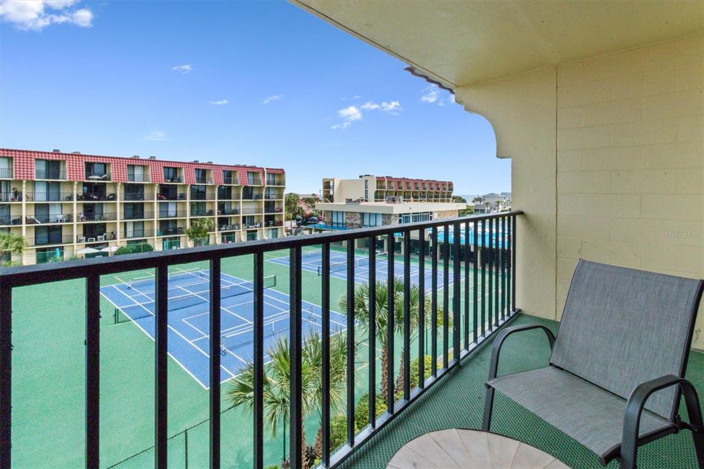 A balcony with a chair and table overlooks tennis courts and a multi-story building — 1433 N ATLANTIC AVENUE UNIT 422, DAYTONA BEACH, FL