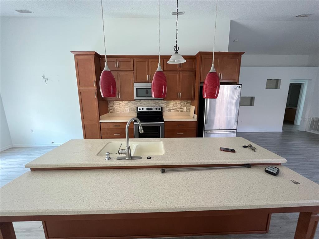 A kitchen features wood cabinets, stainless steel appliances, a large island, and red pendant lights — 10565 ROCKING A RUN, ORLANDO, FL