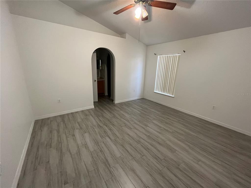 A bedroom with white walls, gray wood-look flooring, a vaulted ceiling, and an arched doorway — 10565 ROCKING A RUN, ORLANDO, FL