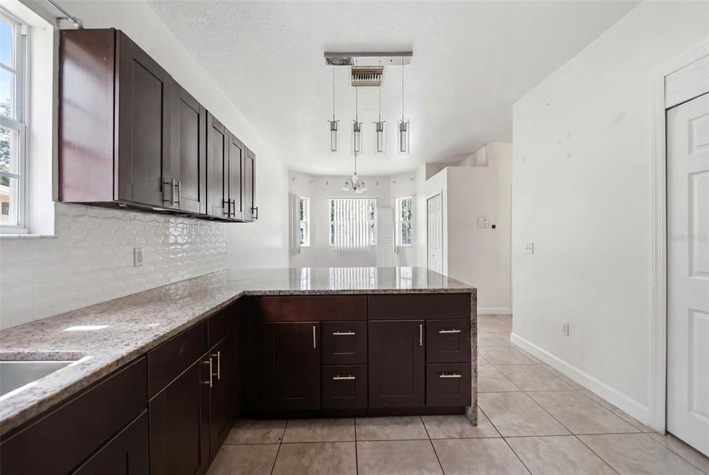 A kitchen features dark wood cabinets, granite countertops, a tiled backsplash, and a breakfast bar — 4404 AMERICA STREET, ORLANDO, FL