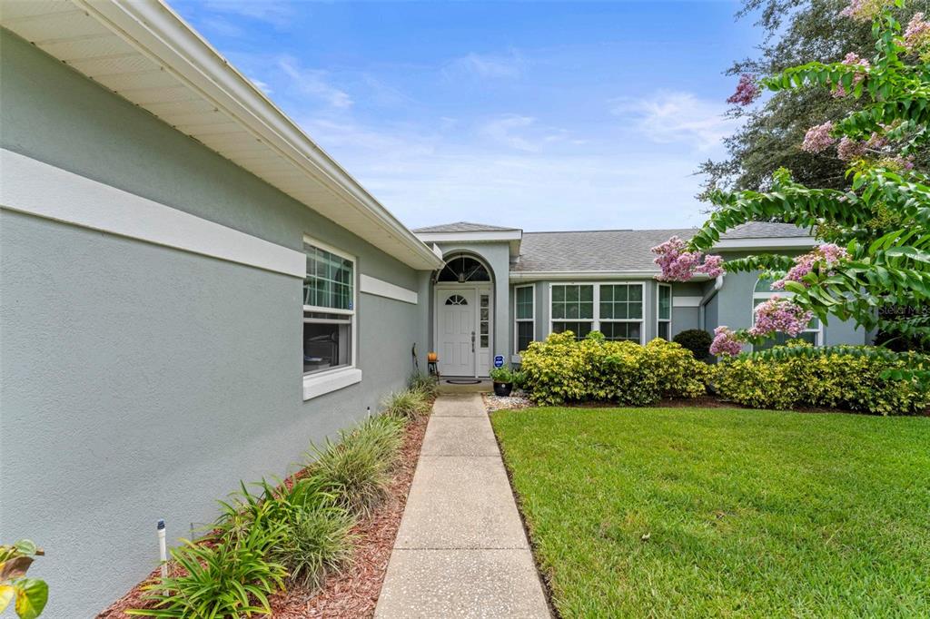 A concrete walkway leads to the front entrance of a single-story house with gray siding — 11218 FOUNTAIN LAKE BOULEVARD, LEESBURG, FL