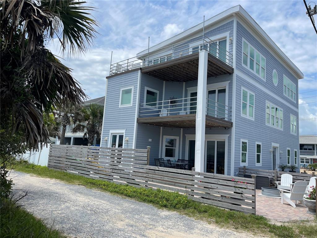 A three-story blue house features stacked balconies and a gravel driveway behind a wooden fence — 1501 S CENTRAL AVENUE, FLAGLER BEACH, FL