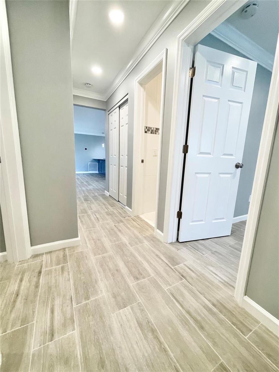 A hallway with light wood-look tile flooring leads to a room with blue cabinets — 3509 NW 25th Way, Boca Raton FL 33434, BOCA RATON, FL