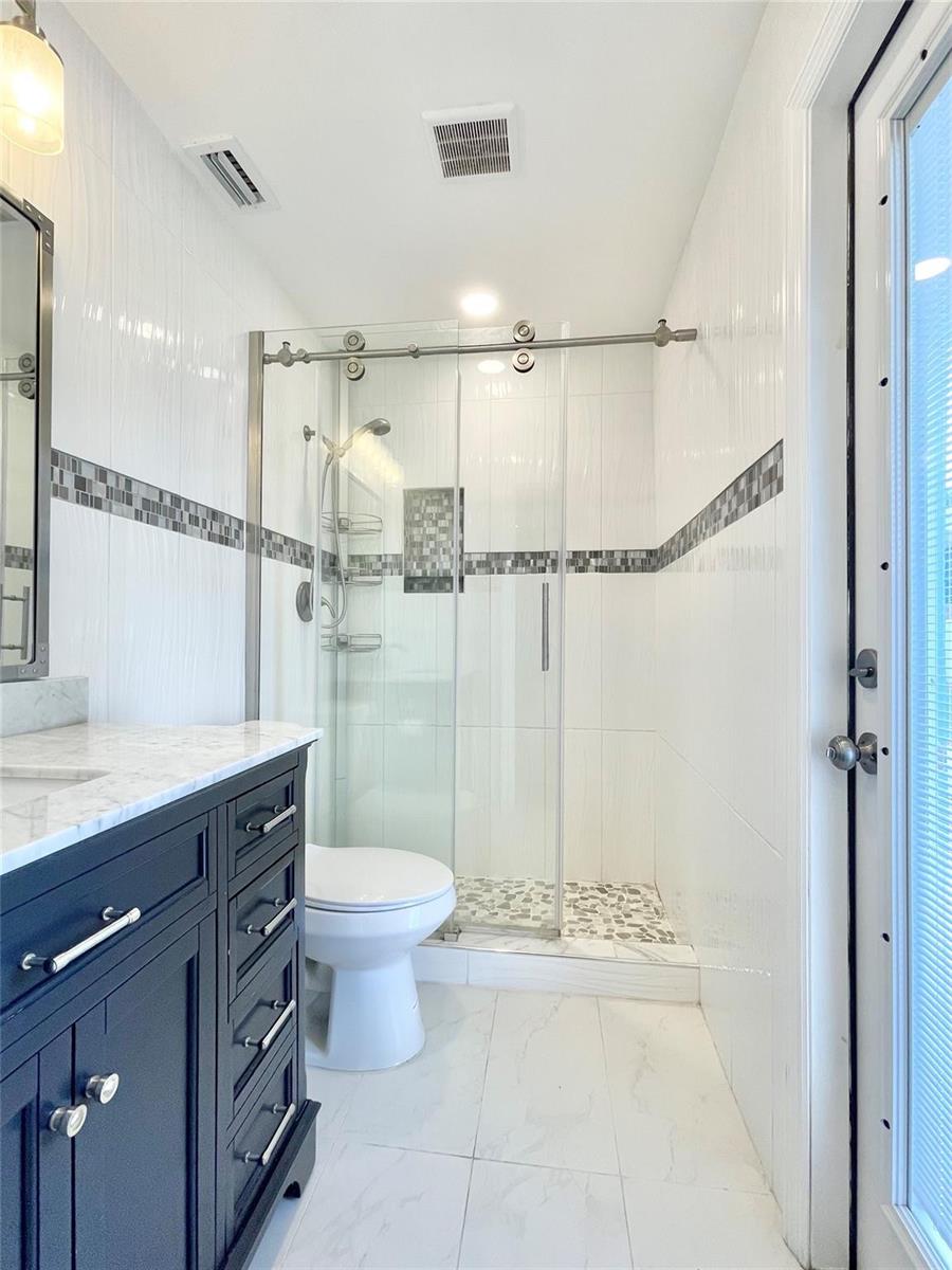 A bathroom features a dark vanity, white tile walls with mosaic accents, and a glass shower — 3509 NW 25th Way, Boca Raton FL 33434, BOCA RATON, FL