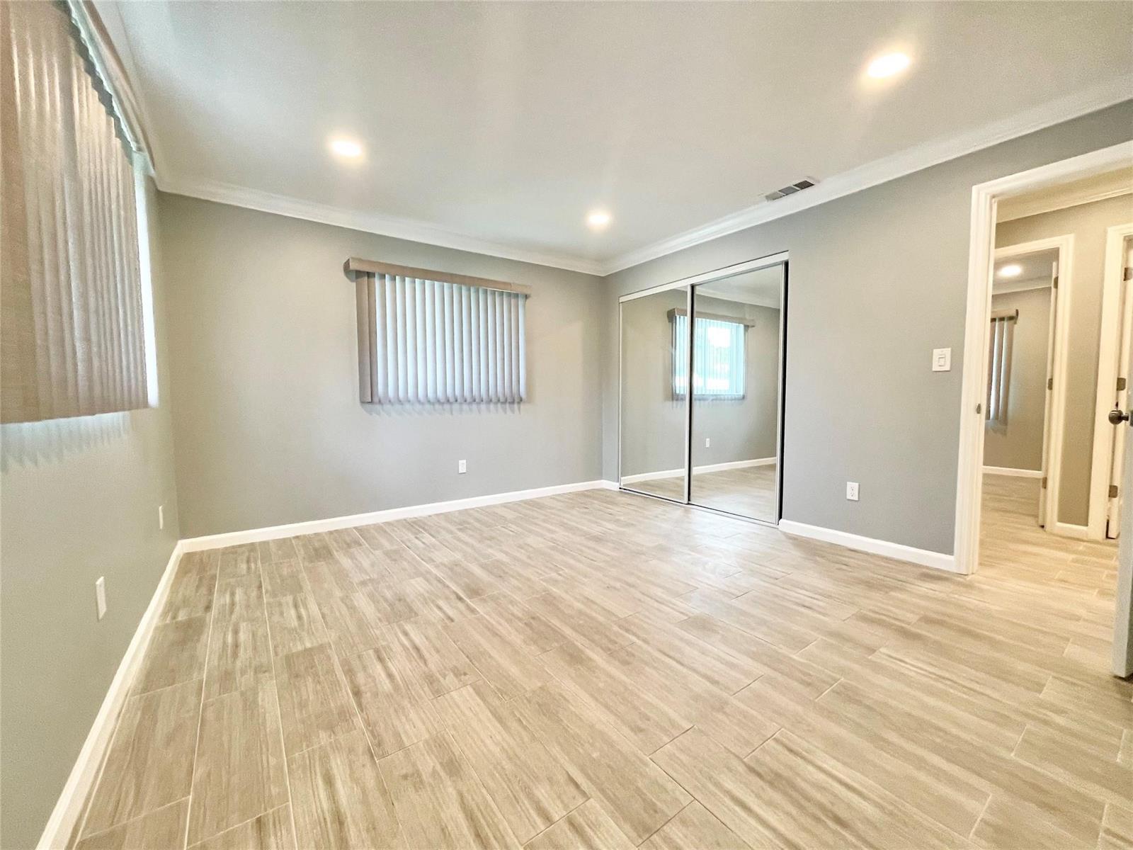 A bedroom with light gray walls, wood-look tile flooring, and mirrored sliding closet doors — 3509 NW 25th Way, Boca Raton FL 33434, BOCA RATON, FL