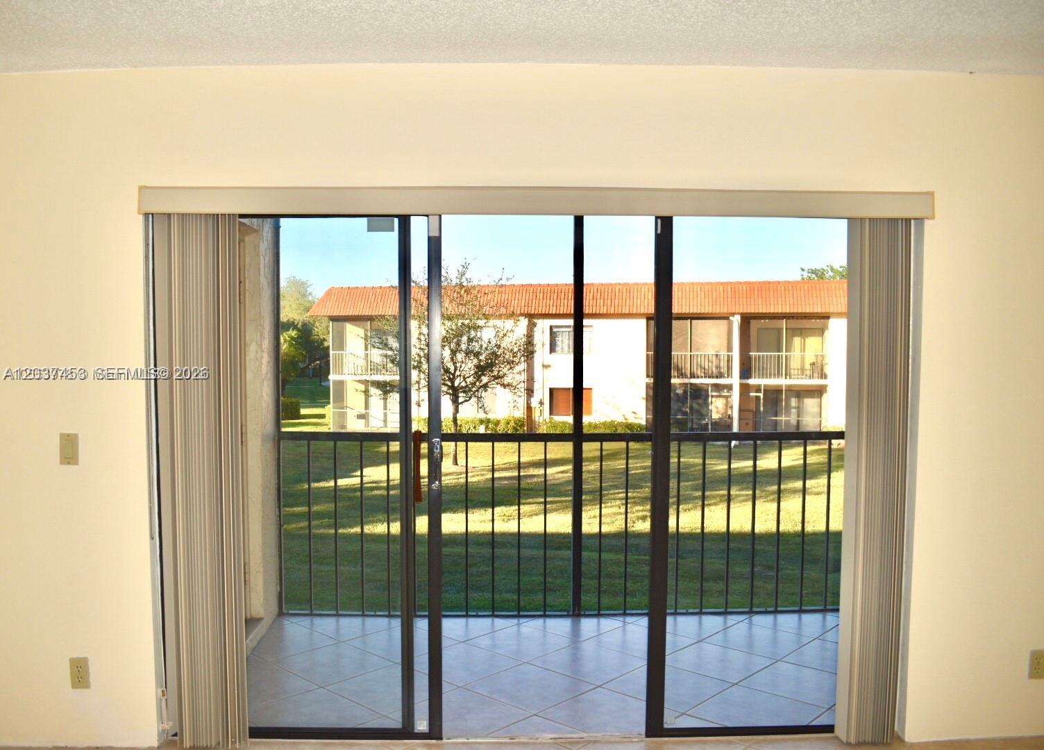 A view through a sliding glass door onto a screened balcony overlooking a courtyard — 369 Lakeview Dr # 204, Weston FL 33326, WESTON, FL