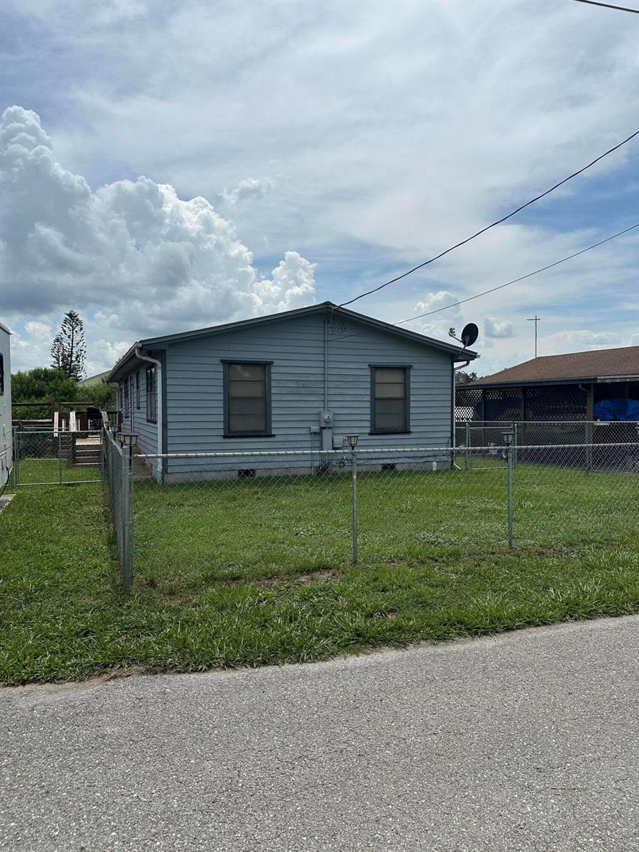 A blue, single-story house with two windows and a chain-link fence in the yard — 1110 3rd Street, Okeechobee FL 34974, OKEECHOBEE, FL