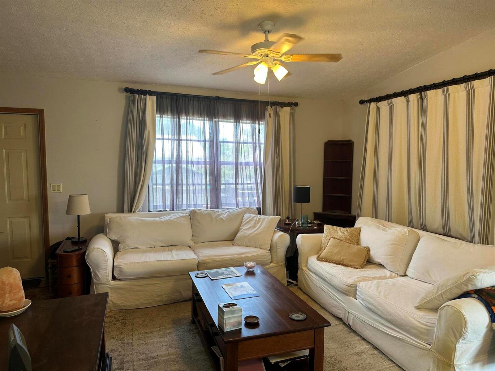 A living room features two white sofas, a wooden coffee table, and striped floor-length curtains — 1110 3rd Street, Okeechobee FL 34974, OKEECHOBEE, FL