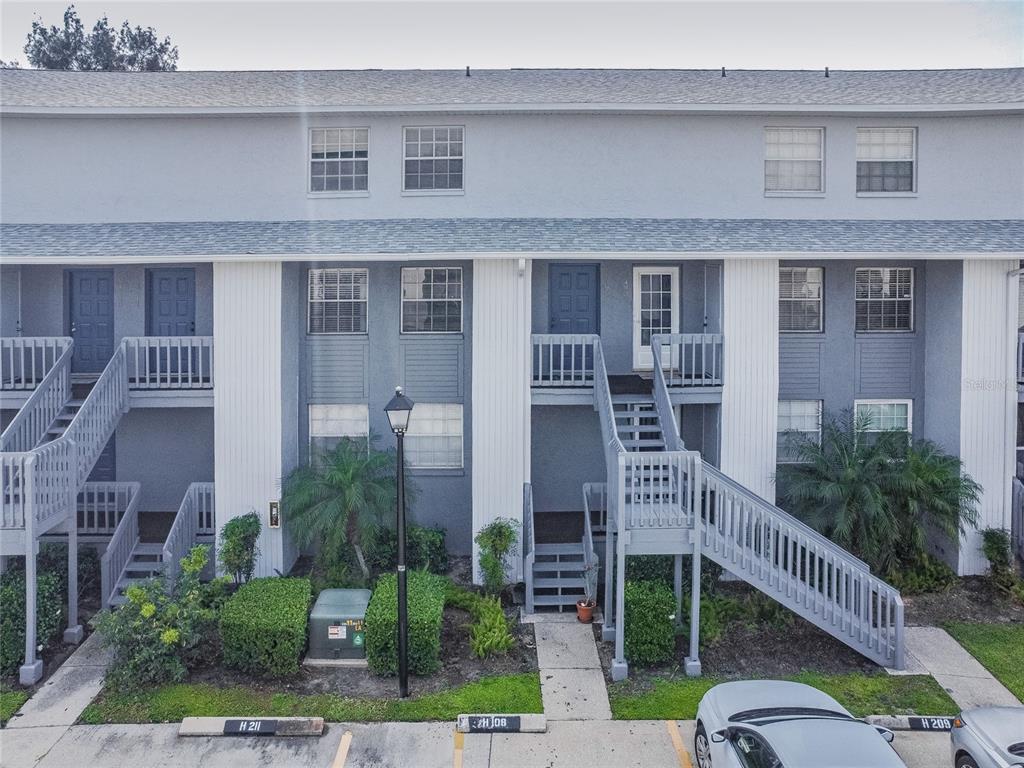 An exterior view of a multi-story apartment building with gray siding and wooden staircases — 4907 W MCELROY AVENUE UNIT H209, TAMPA, FL