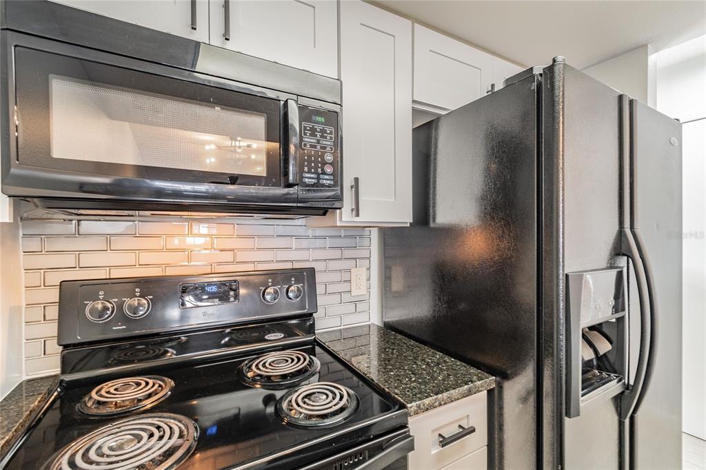 A kitchen features black appliances, white cabinets, a subway tile backsplash, and dark granite countertops — 4907 W MCELROY AVENUE UNIT H209, TAMPA, FL